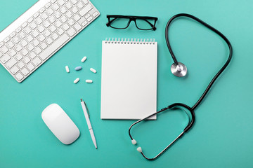 Stethoscope in doctors desk with notebook, pen, keyboard, mouse and pills