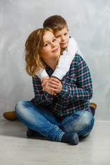 Beautiful woman and her cute little son are touching their noses and smiling, on gray background