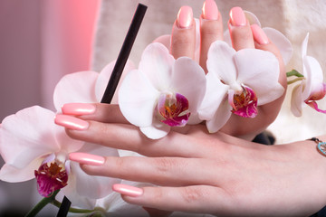Young woman hands with pink spring manicure on nails holding white orchids flower in hands in beauty salon. Manicure and Beauty concept. Close up, selective focus