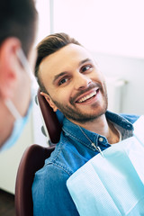 Pretty face mimic and a white smile of a nice man in a dental chair after getting a doctor’s treatment  in a professional clinic.