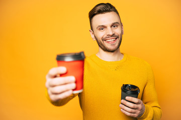 Two cups of coffee or tea in cups of red and black colors in hands of nice-looking man clothed in...