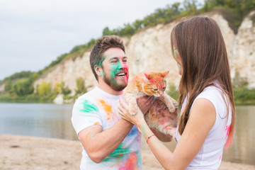 Obraz premium Festival holi , tourism and nature concept - Portrait of woman and man with cat covered multi-colored dust