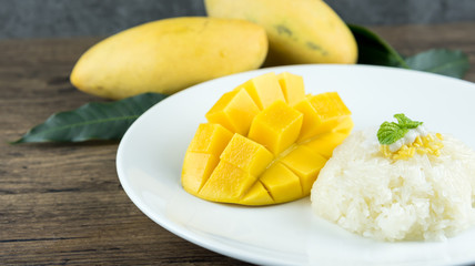 The close up of heap yellow mango and sticky rice setting with coconut milk in the dish on wooden table. popular traditional dessert of Thailand.