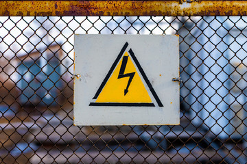 A sign warning of the dangers of high electrical voltage hangs on the mesh fence that surrounds the power line substation.