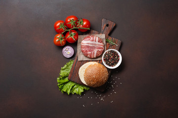 Hamburger ingredients raw cutlet, tomatos, lettuce, bun, cheese, cucumbers and onion on rusty background