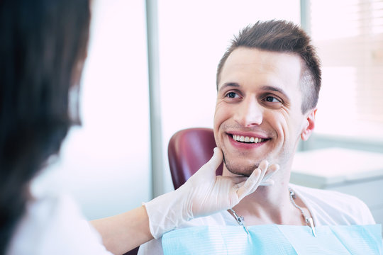 The absolute finito. A man with a beautiful perfect and white smile made with a help of a dentist who is sitting in front of he and making an examination of her work.