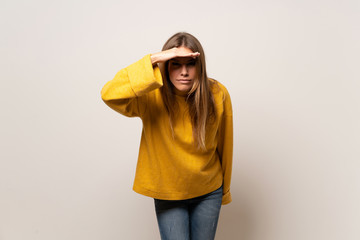 Woman with yellow sweater over isolated wall looking far away with hand to look something