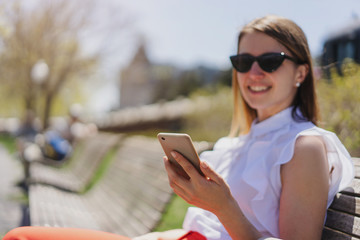 Happy woman spending free time in break on a bench while using smart phone in sunny day