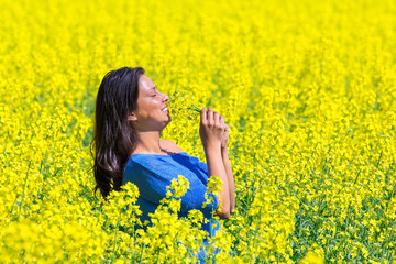 Young woman smells yellow flowers in rapeseed field
