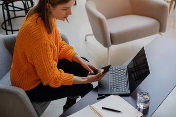 Business woman using smartphone while working on laptop in co-working place, Woman wearing in...