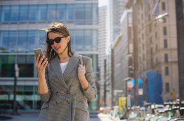 Happy successful business woman making video call outdoor, smiling female entrepreneur talking via mobile phone and walking on the business city centre