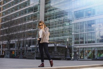 Obraz premium Young stylish girl talking via smartphone in downtown, Stylish blogger walking while calling her friends via smart phone