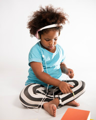 Afro-American little girl with headphones listening to music on white background