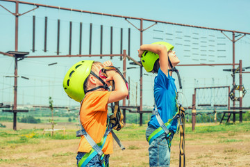 Two children in helmets and safety gear are looking up in an extreme park.