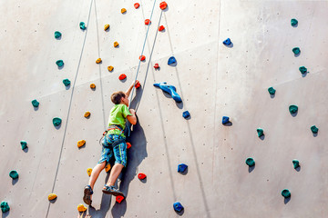 The boy climber climbs on an artificial tower, overcoming obstacles on his way up.