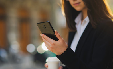 Cropped image of female hands holding smartphone, Business woman using smart phone while drinking coffee outside