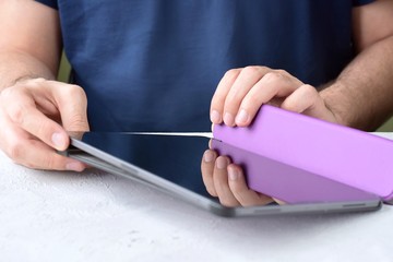 White man‘s hands holding a new tablet and put on a purple leather case with selective focus. Man using a tablet. Putting on a violet protection cases for personal tablet. Tablet accessories
