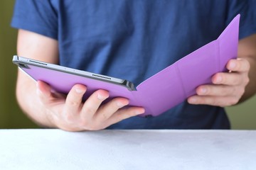 White man‘s hands holding a new tablet and put on a purple leather case with selective focus. Man using a tablet. Putting on a violet protection cases for personal tablet. Tablet accessories