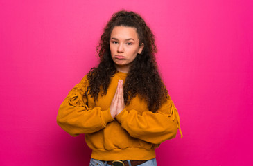 Teenager girl over pink wall keeps palm together. Person asks for something