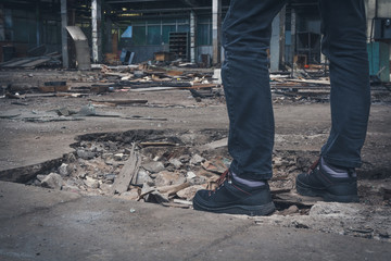 A man in black clothes stands on the rubble in an old abandoned building