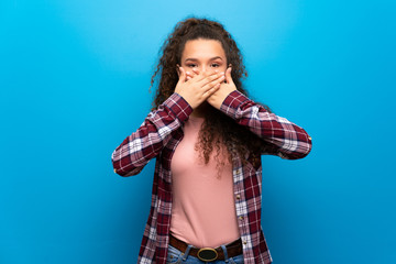 Teenager girl over blue wall covering mouth with hands for saying something inappropriate