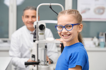 Teenage girl in blue glasses posing with doctor in clinic.