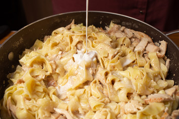 Cooking pasta at home. adding cream to cooked pasta in a pan.Close-Up