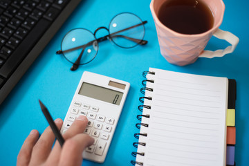 Office desk with other supplies and male hand using calculator.