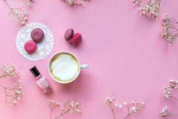 Flatlay pink coral background, the cup of cappuccino coffee and sweets macaroons, spring white flowers