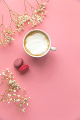 Obraz na płótnie Canvas Flatlay pink coral background, the cup of cappuccino coffee and sweets macaroons, spring white flowers