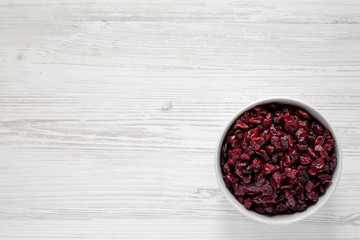 Dry organic cranberries in a gray bowl over white wooden surface, top view. Overhead, from above, flat lay. Copy space.