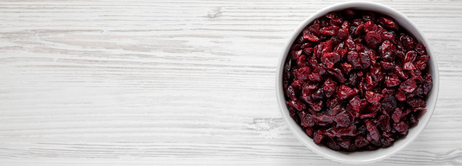 Full bowl of dry organic cranberries on a white wooden table, top view. Overhead, from above, flat lay. Copy space.
