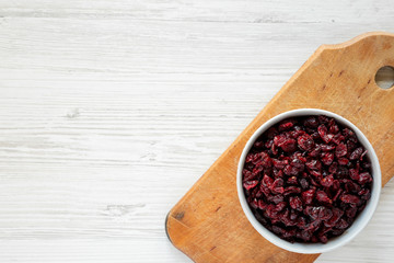 Dry organic cranberries in a gray bowl on rustic board over white wooden background, top view. Overhead, from above, flat lay. Copy space.