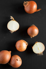 Unpeeled raw yellow onions on black background, top view. Flat lay, overhead, from above. Close-up.