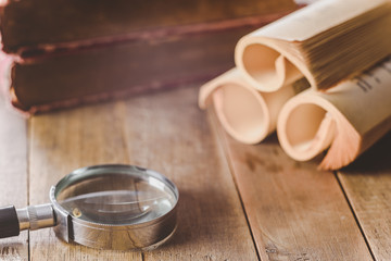 close-up of magnifying glass on wooden table and old books background