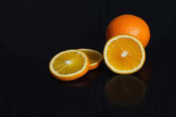 Halved and whole oranges over black background, side view. Space for text.