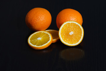 Halved and whole oranges over black background, side view. Space for text.