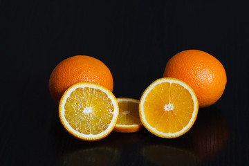 Halved and whole oranges over black background, side view. Space for text.