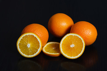 Halved and whole oranges over black background, side view. Space for text.