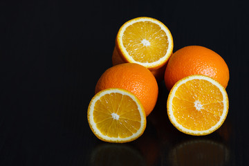 Halved and whole oranges over black background, side view. Space for text.