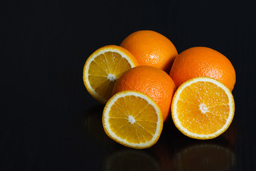 Halved and whole oranges over black background, side view. Space for text.