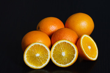 Halved and whole oranges over black background, side view. Space for text.