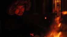 Funny smiling young man warm hands an open fireplace outdoor at night happy in winter mountains burn firewood wood black nature smoke heat orange camp evening fun wild cold relax travel slow motion