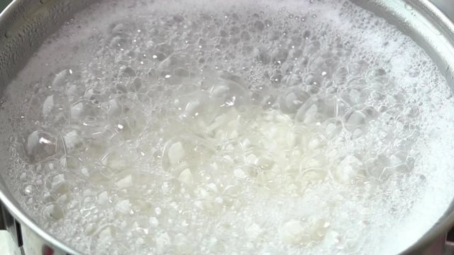 Slow motion surfact of boiling water to cook rice in a stainless steel pot at the kitchen