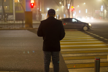 Rear view of a man going home late at night. The guy crosses the road at a pedestrian crossing.