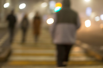 Blurred background of the road, rear view, people go home late at night. People cross the road at a pedestrian crossing.