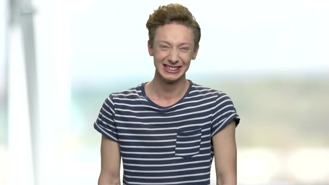 Teenage boy in t-shirt laughing hysterically. Nervous teen guy with emotional face expression. Abstract blurred background.