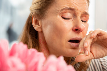 Aged woman with facial wrinkles sneezing after smelling bouquet