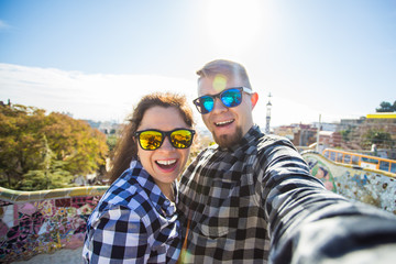 Funny young couple looking at camera taking photo with smart phone smiling in Park Guell, Barcelona, Spain.