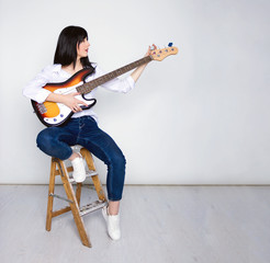 Girl sitting and tune bass guitar, gray background